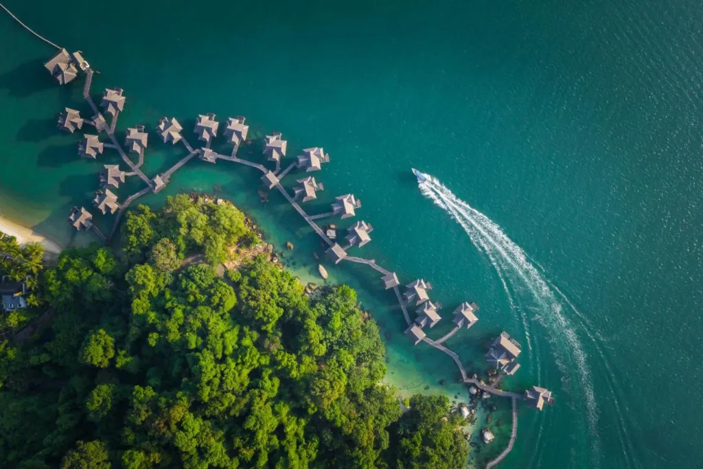 Aerial view of an exclusive overwater bungalow resort near Pangkor Island, Malaysia, featuring turquoise waters and lush jungle. Book ultra-luxury Malaysia holidays, honeymoons, or bespoke travel tours with our specialist DMC.