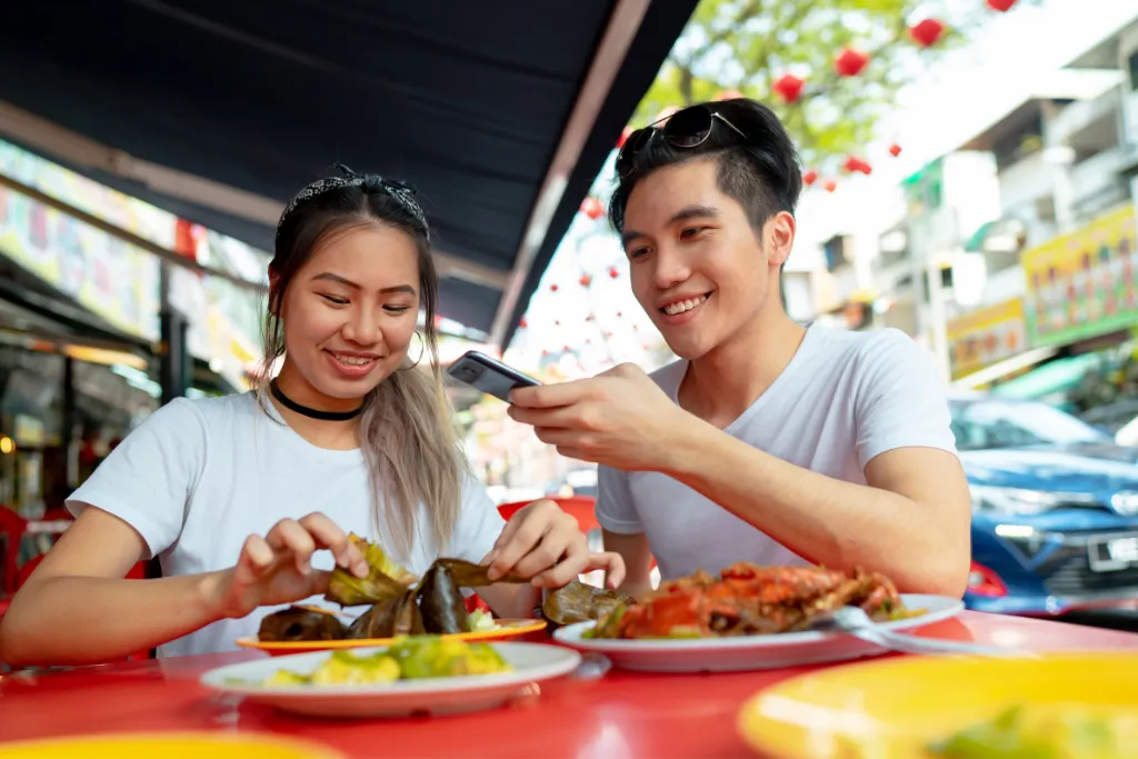 Young travelers enjoying authentic Malaysian hawker food, including seafood and traditional street snacks, in Kuala Lumpur. Promote this culinary experience as part of luxury Malaysia tours and bespoke DMC travel holidays.