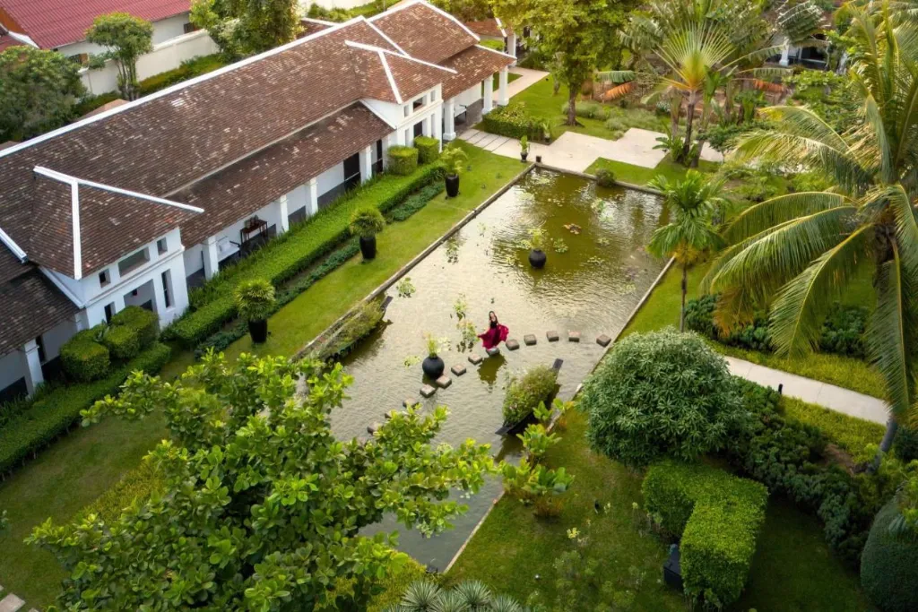 An aerial view of a colonial-style luxury resort in Luang Prabang, Laos, featuring long, elegant buildings, manicured gardens, and a tranquil pond. The perfect high-end base for your Laos tours and customized Laos holidays.