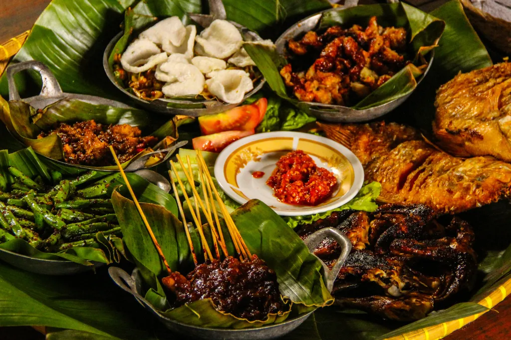 A delicious spread of authentic Indonesian food, featuring grilled Satay skewers, fried fish, spicy Sambal, and crackers. Discover the rich flavors on our exclusive Indonesia Culinary tours and Luxury dining experiences.