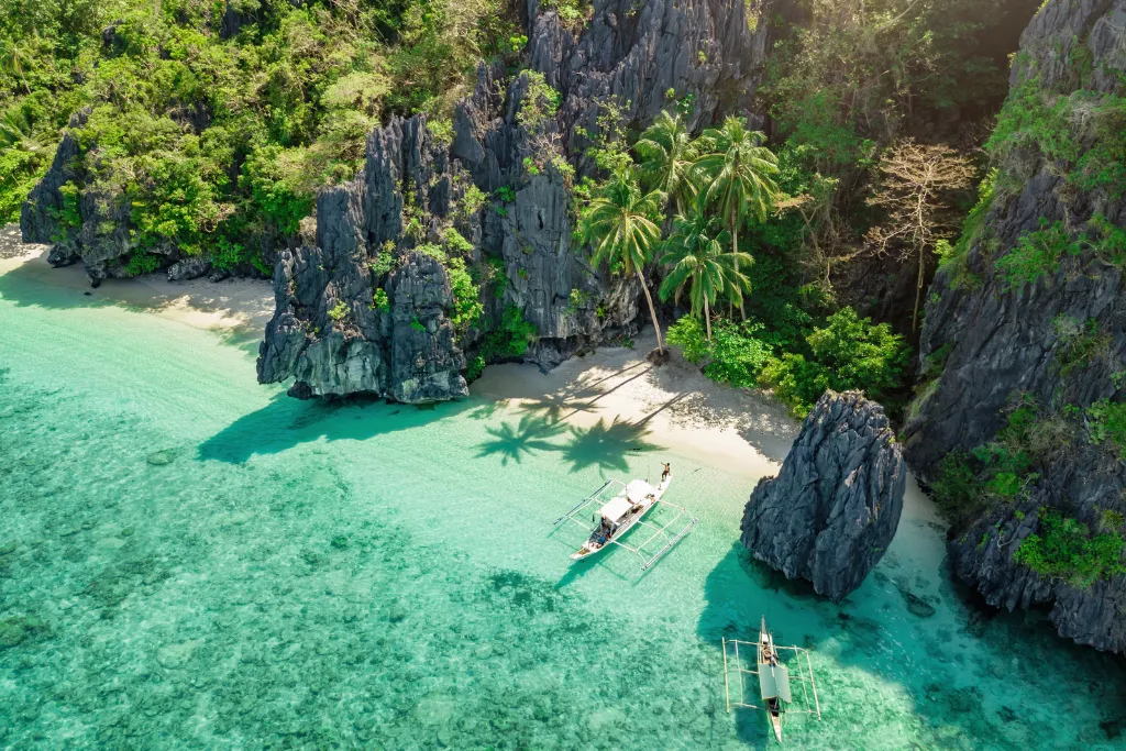 Aerial view of a secluded beach in El Nido, Palawan, with limestone cliffs and turquoise water. The perfect setting for luxury Philippines tours, island hopping, and exclusive travel.