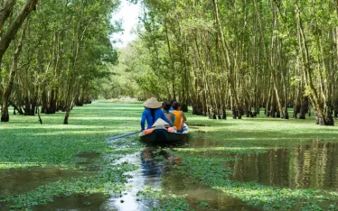 A small boat with local guides paddles through the serene, submerged forest of the Mekong Delta, Vietnam. Experience authentic South Vietnam travel and eco-tourism with personalized Mekong Delta tours from our expert Vietnam DMC.