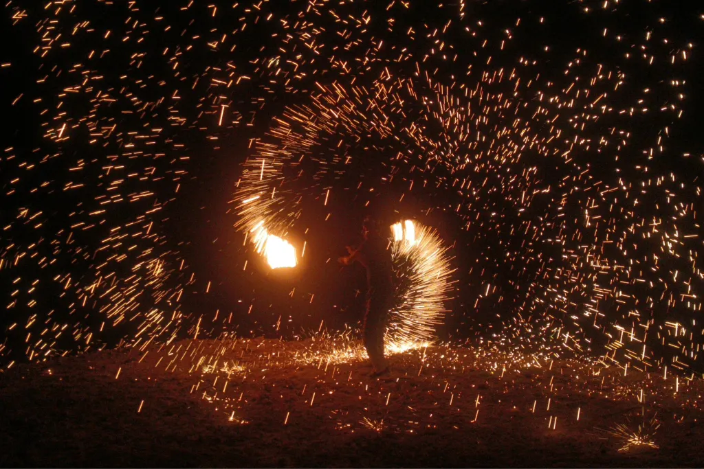 Spectacular fire dancer performance creating a shower of sparks on a Philippine island beach at night. Experience the vibrant nightlife on luxury Philippines travel and holidays.