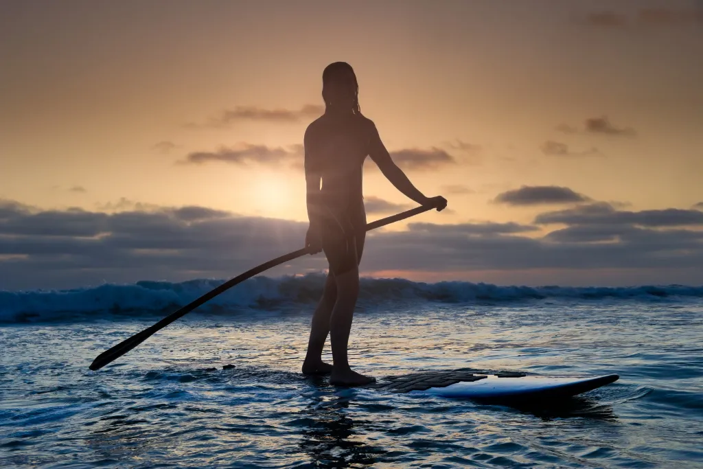 Silhouette of a paddleboarder on the water at sunset in the Philippines. Highlight great water activities and serene moments on your next Philippines adventure holidays or luxury tours.