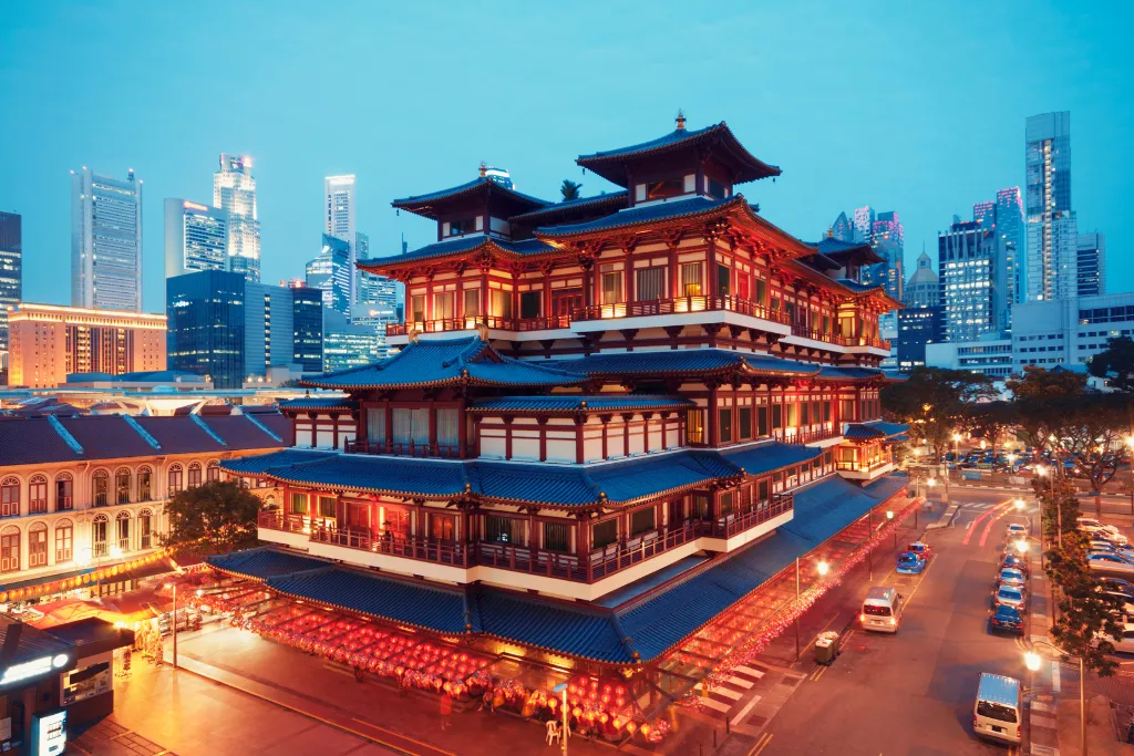 The illuminated Buddha Tooth Relic Temple in Singapore's Chinatown set against the modern skyline.