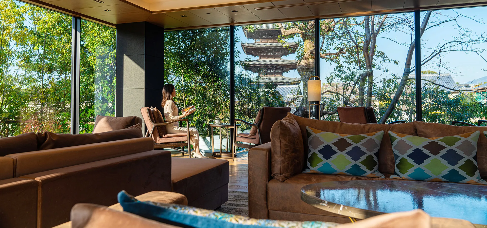 kyoto-luxury-hotel-lounge-pagoda-view-day Daytime Kyoto hotel lounge for luxury travel in Japan. Features a woman relaxing, plush seating, and pagoda view through expansive windows.