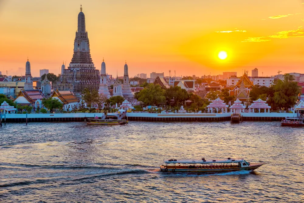 Stunning sunset over Wat Arun (Temple of Dawn) in Bangkok, with a longtail boat cruising the Chao Phraya River. Perfect view for a luxury Bangkok itinerary.