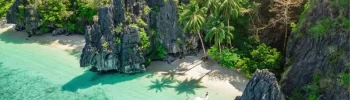 An aerial view of a private, crystal-clear turquoise cove in Palawan, featuring traditional outrigger boats and dramatic limestone cliffs—curated by an expert Philippines travel operator for luxury island-hopping itineraries.
