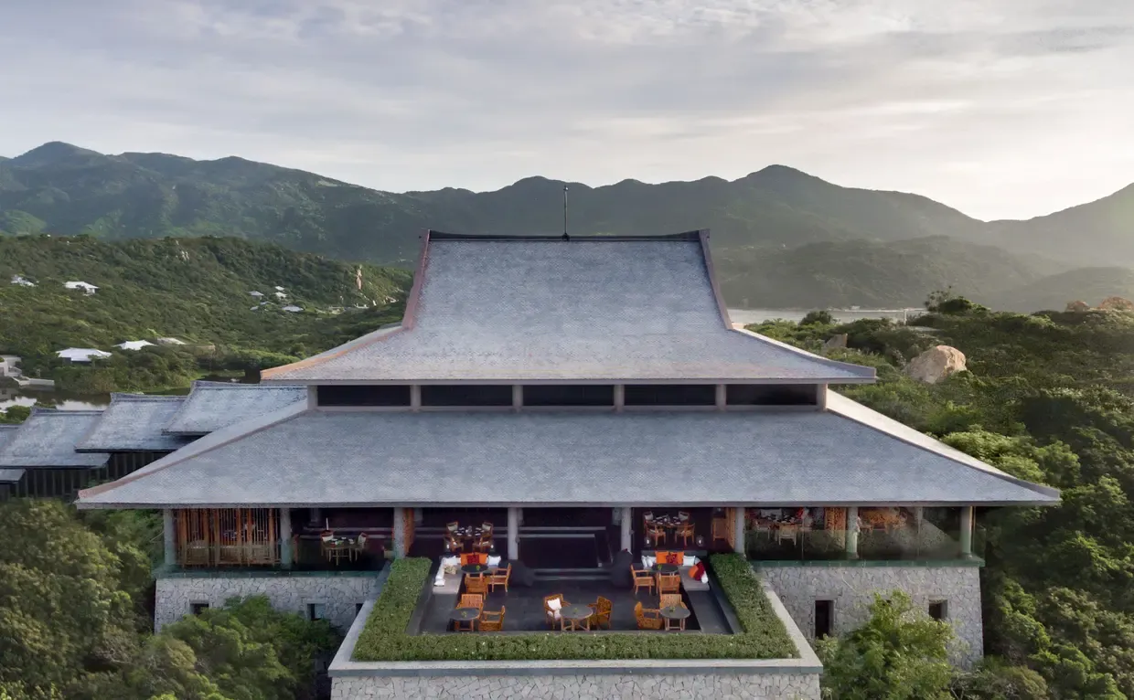 Aerial view of Amanoi resort's open-air dining pavilion with sweeping traditional Vietnamese roofline, nestled among lush jungle hills overlooking the coast of Ninh Thuan, Vietnam