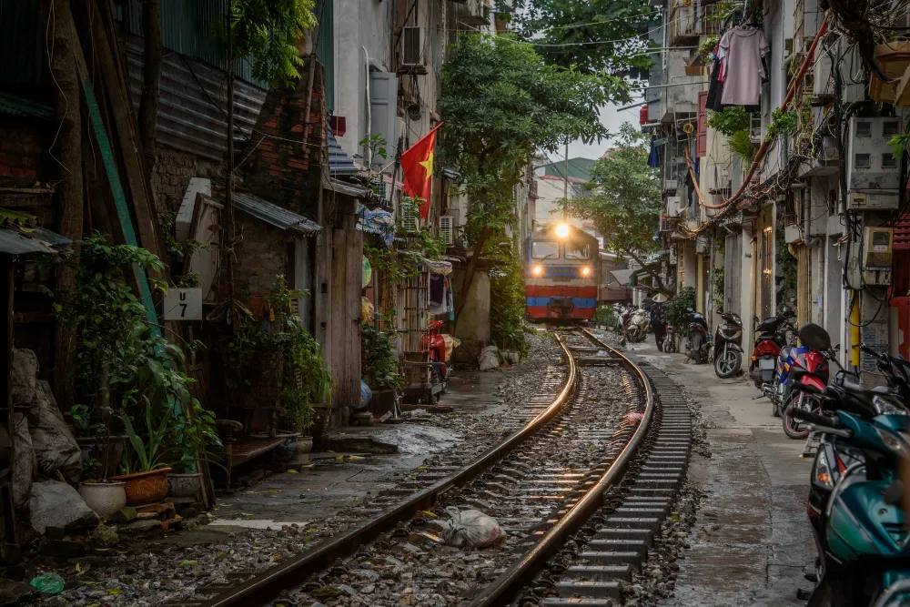 A train easing through Hanoi's narrow Train Street, tracks running between close-set houses in the Old Quarter