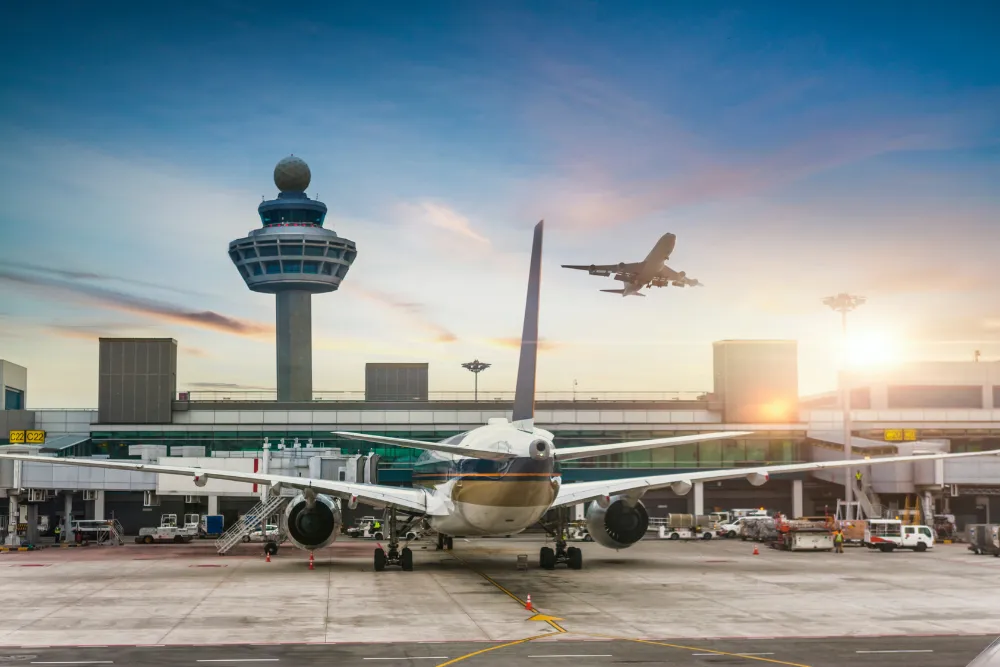 Aircraft on the tarmac at Singapore Changi Airport, with the control tower and another plane departing at sunset