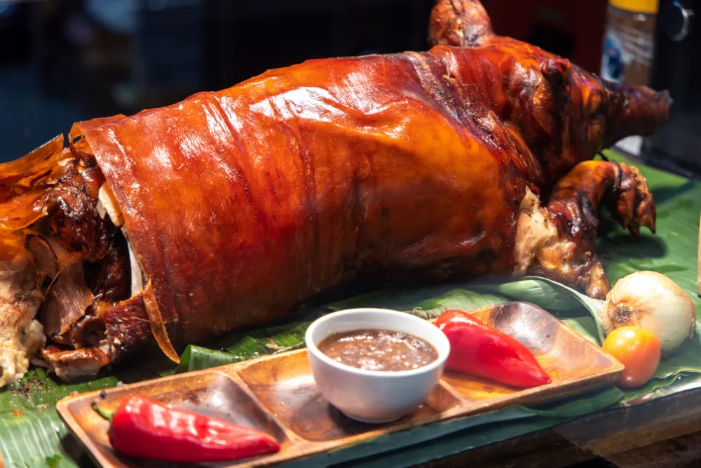 Whole roasted Filipino lechon served on banana leaves with dipping sauce, highlighting traditional food experiences in the Philippines.