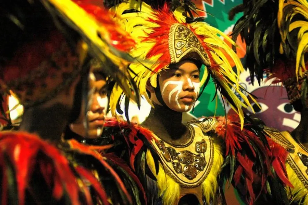 Tribal street dancer with facial paint and a vibrant yellow and red feathered headdress performing at the Dinagyang Festival,