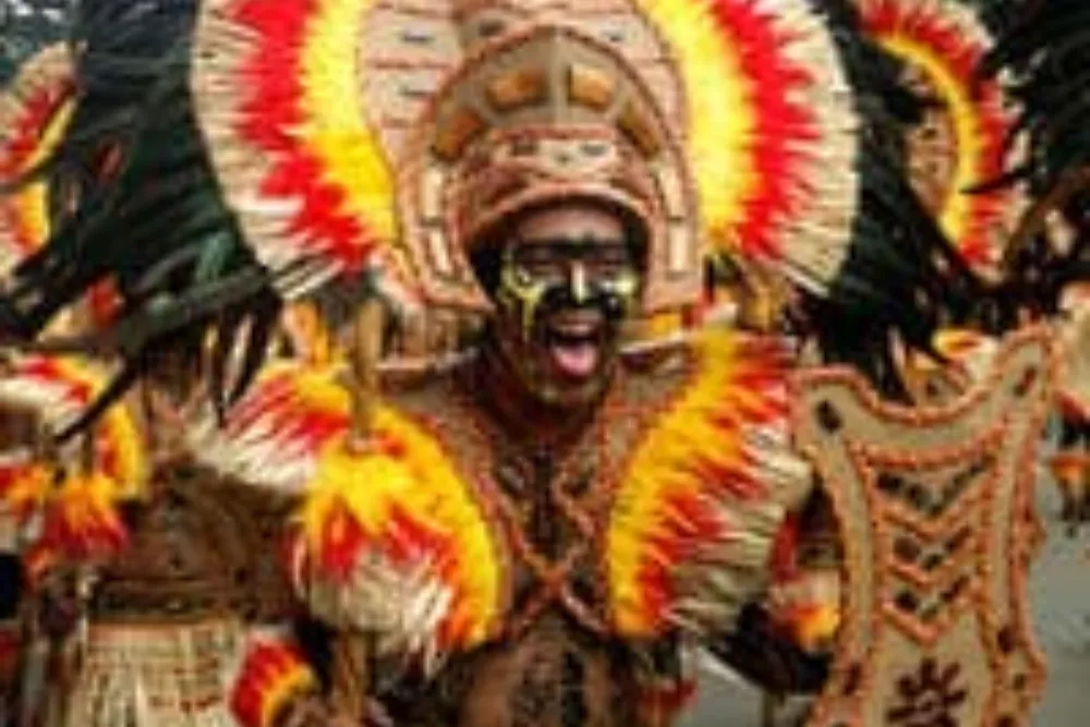 Performer in colorful feather headgear and face paint celebrating during a festival street dance, featured on Philippines cultural tours.