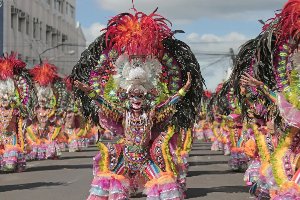 Street performers in elaborate feather headdresses and smiling masks dancing at the MassKara Festival in Bacolod City, managed by a Philippines DMC.