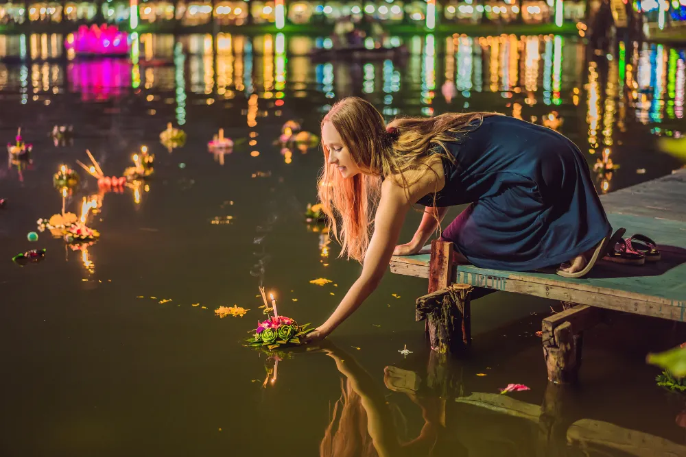 Tourist releasing a lit floral krathong onto the water during Loy Krathong festival on Thailand tours.