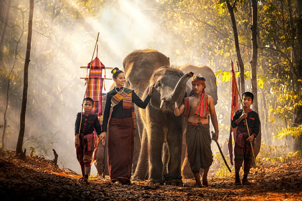 Thai family in cultural clothing walking alongside elephants through the forest on authentic Thailand tours.