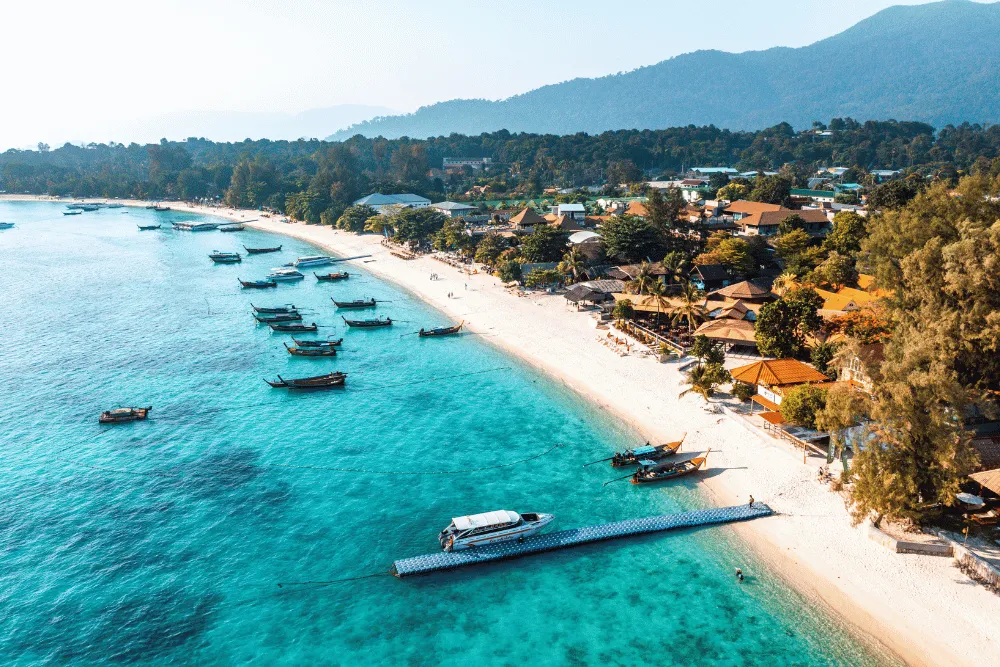 Thailand island hopping tour showcasing clear blue ocean, white sandy beach, floating pier, and longtail boats.